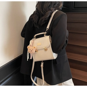 Detail of cream PU leather backpack with gold buckle and brown bear charm on model