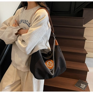 Detail of black nylon hobo bag featuring orange leather logo patch and silver chain strap