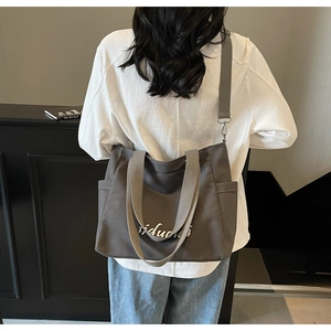 Gray canvas tote bag detail with wide strap and white script print on minimalist surface