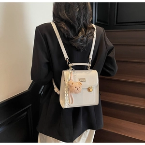 Detail of cream mini leather backpack featuring a plush bear charm and metallic clasp