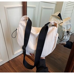 Mirror view of a cream nylon crossbody bag with wide black strap and drawstring detail
