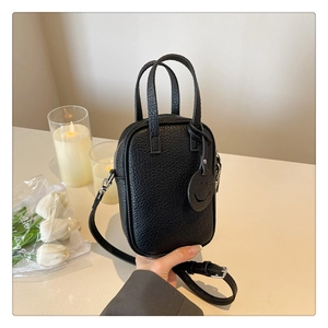 Close-up of black pebble grain leather texture on mini crossbody bag with smiley charm