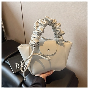 Detail of a creamy beige pleated handbag with decorative bow and magnetic flap closure