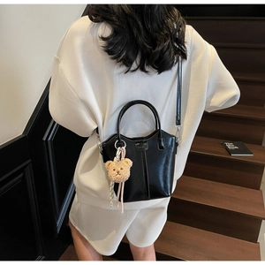 Close-up of black glossy bucket bag with long strap and a brown plush bear charm