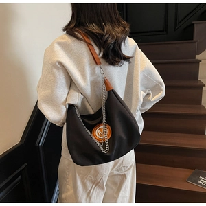 Hobo bag worn by model featuring nylon body, brown leather strap and silver chain details