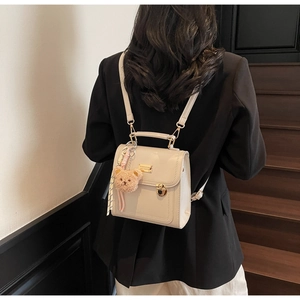 Detail of cream backpack with gold clasp and brown teddy bear charm on model
