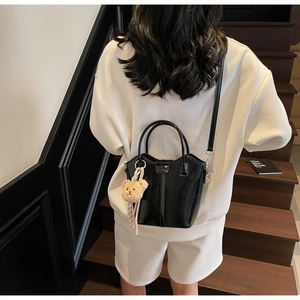 Model carrying a black patent leather bucket bag with a cute plush bear charm detail