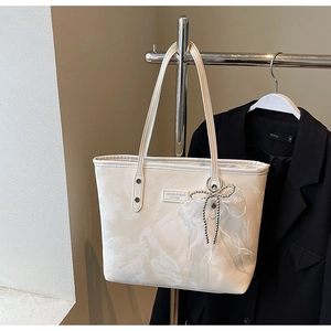 Detail einer cremefarbenen Schultertasche mit Marmormuster, Schleife und Perlenkette