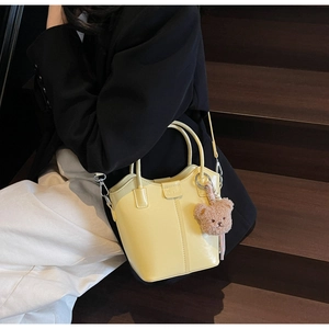 Detail of yellow bucket bag featuring a round handle and a cute plush bear charm
