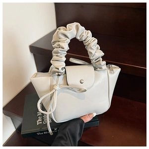 Detail of ruched handle and bow decoration on the light gray trapezoid handbag
