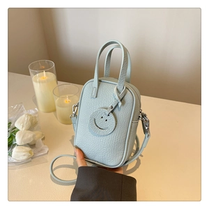 Close-up of light blue pebbled leather mini crossbody bag with cute smiley face charm