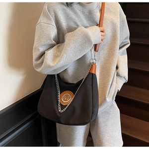 Detail of black nylon crescent bag with orange M logo and silver chain strap details