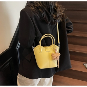 Detail of yellow bucket bag with plush bear charm and adjustable strap on a dark blazer