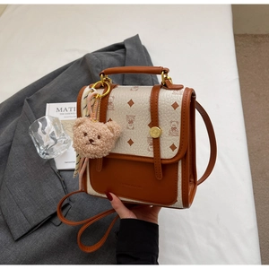 Detail of vintage patchwork handbag with bear print pattern and plush charm on white surface