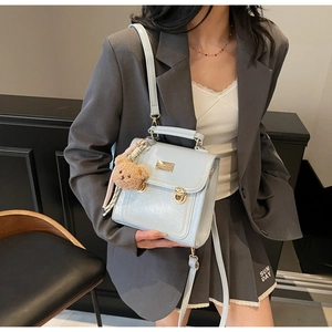Close-up of ice blue crossbody bag with bear charm and pearl strap on model
