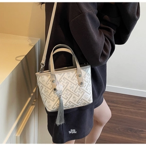 Detail of a mini bucket bag featuring gray floral jacquard pattern and long tassel charm