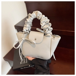 Close-up of a cream pleated handbag featuring a scrunchie handle and decorative bow knot