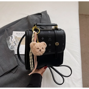 Detail of black textured leather backpack featuring bear pattern and plush bear charm