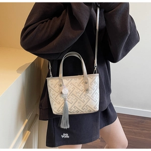 Detail of white mini bucket bag with geometric embroidery and elegant grey tassel charm