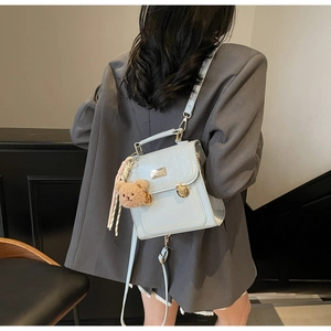 Detail of light blue leather backpack with gold buckle and cute brown bear pendant