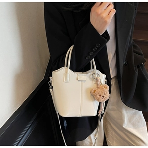 Detail of white glossy bucket bag with cute brown bear charm and long crossbody strap