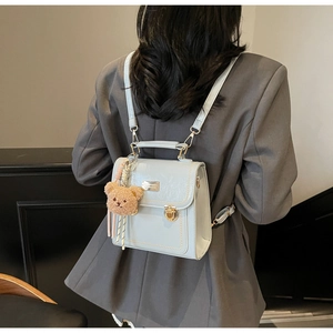 Modella in abito grigio indossa borsa a tracolla azzurra come zaino con ciondolo a orsetto
