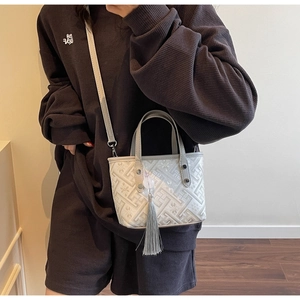 Detail of floral textured mini bucket bag featuring a grey silk tassel charm and strap