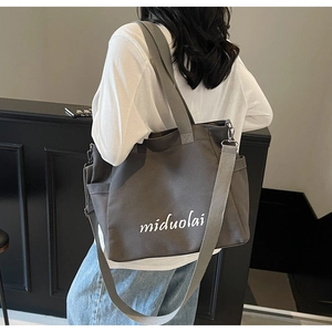 Detail of dark grey canvas tote bag with white script logo worn by a model in casual style