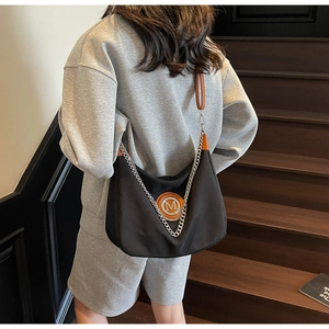 Detail of black nylon crossbody bag with metal M logo and brown leather strap on model