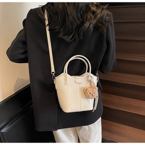 White glossy bucket bag with brown teddy bear charm on a model at wooden stairs