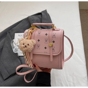 Detail of pink PU leather handbag with litchi texture, gold buckle, and plush bear charm