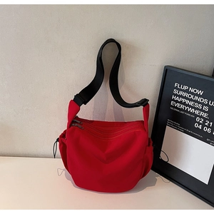 Detail of red canvas crossbody bag showing three front silver zippers and adjustable strap