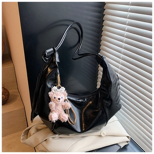 Detail of a black glossy crescent shoulder bag featuring a pink plush bear charm accessory