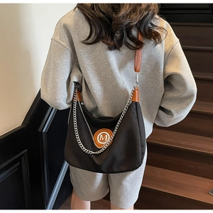 Detail of black dumpling crossbody bag featuring brown leather strap and silver chain