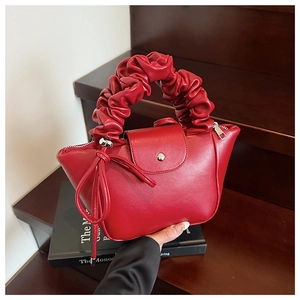 Detail view of red pleated faux leather handbag with cloud handle on wood background