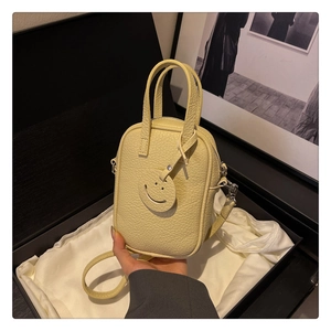Macro view of yellow lychee leather mini crossbody bag with a smiley face charm in box