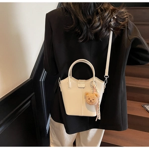 Cream bucket bag with plush bear charm worn crossbody on a stylish staircase