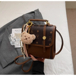 Brown vintage faux leather backpack with plush bear charm on white bedding setup