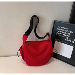 Detail of red nylon crescent crossbody bag featuring side drawstrings and wide black strap