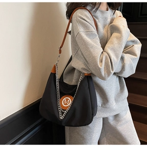 Detail of moon-shaped canvas bag with brown leather strap and silver chain accent