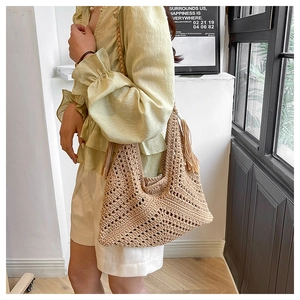 Close-up of a woven straw tote bag with tassel detail and braided shoulder strap