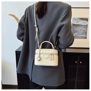 Detail einer cremefarbenen Leder-Kosmetiktasche mit goldener Kette an einem Modell