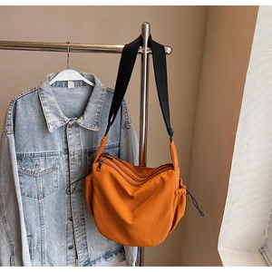 Detailed view of orange canvas crossbody bag with multi-zipper layers and drawstring side pockets