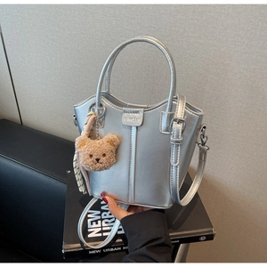 Detail of silver metallic bucket bag with brown plush bear charm on artistic book