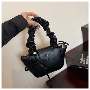 Detail of black pleated handbag featuring a decorative bow knot and secure magnetic closure