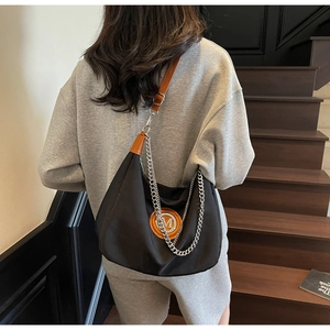 Detail of large black crossbody bag with brown straps and orange metal M logo patch