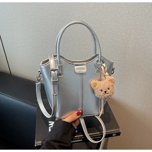 Detail of silver metallic bucket bag with plush bear charm and branding on industrial background
