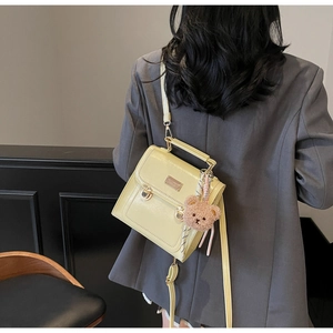 Detail view of cream leather backpack featuring gold buckles and a plush bear charm