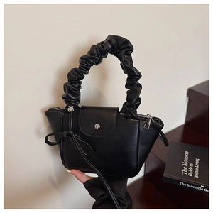 Close-up of black ruched handle and elegant bow charm on a minimalist leather handbag