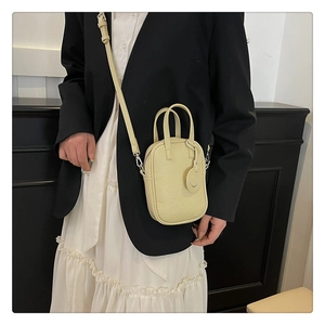 Detail of lychee textured leather mini bag in pale yellow with a smiley face charm